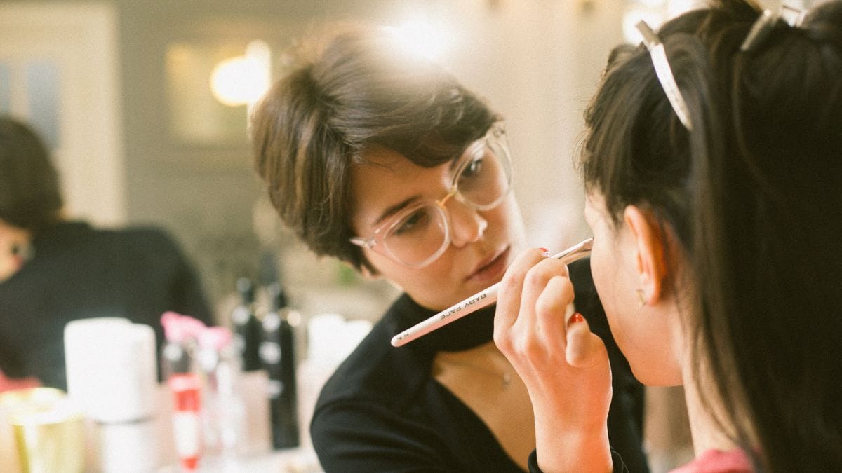 An MUA applies makeup to her client's face at her beauty business.