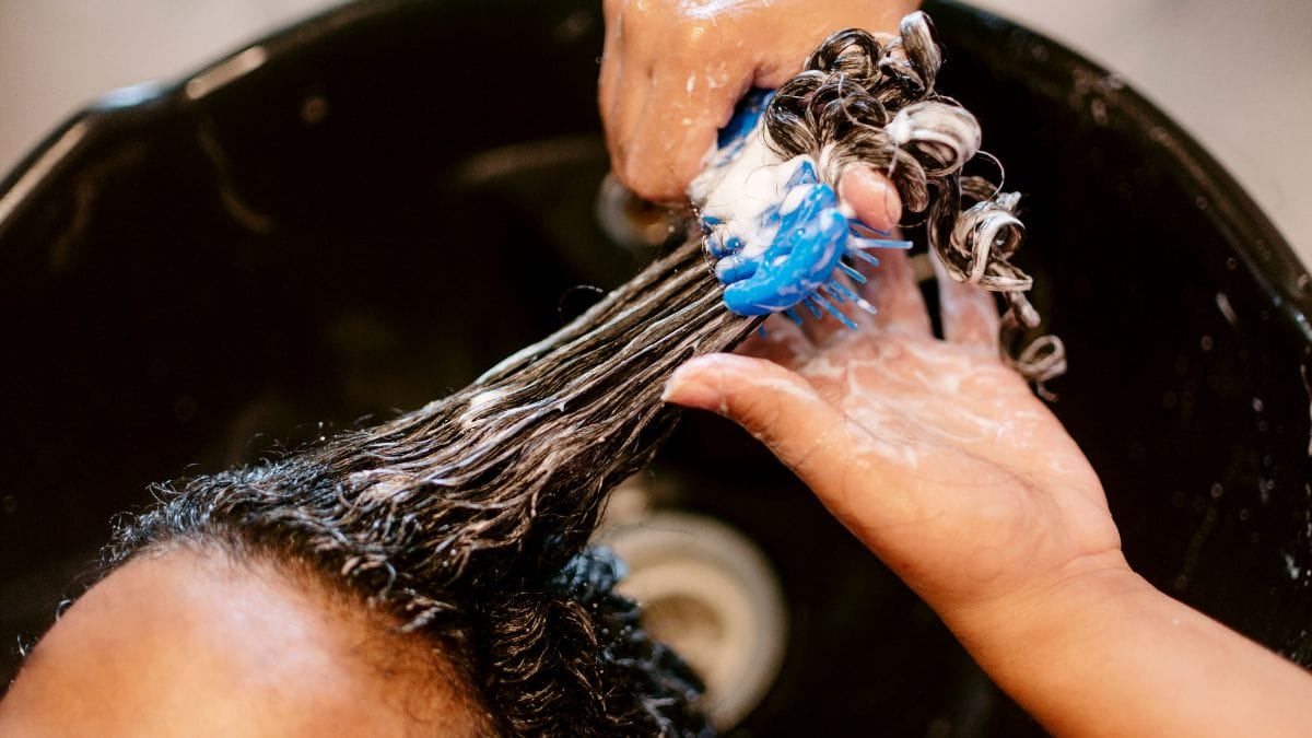 A beauty apprentice washes a client's hair in the shampoo bowl.