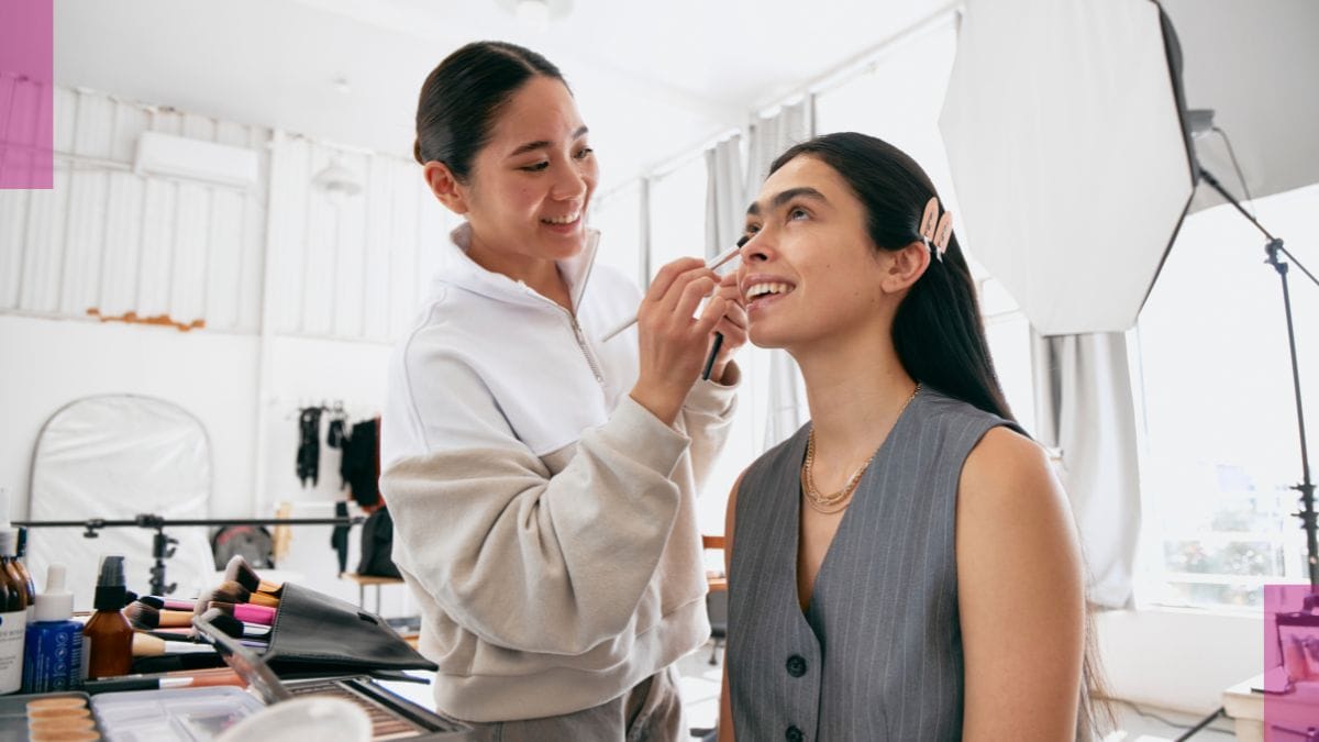 A client smiles as her freelance makeup artist adds blush and highlighter to her face.