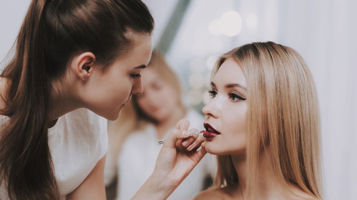 A makeup artist creates the perfect red lip look on her makeup client.