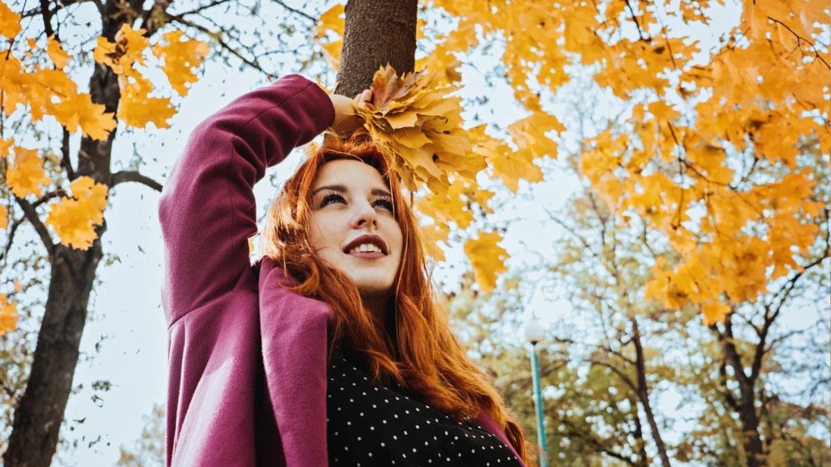 A client with a fresh hair color from her favorite fall salon plays in the autumn leaves.