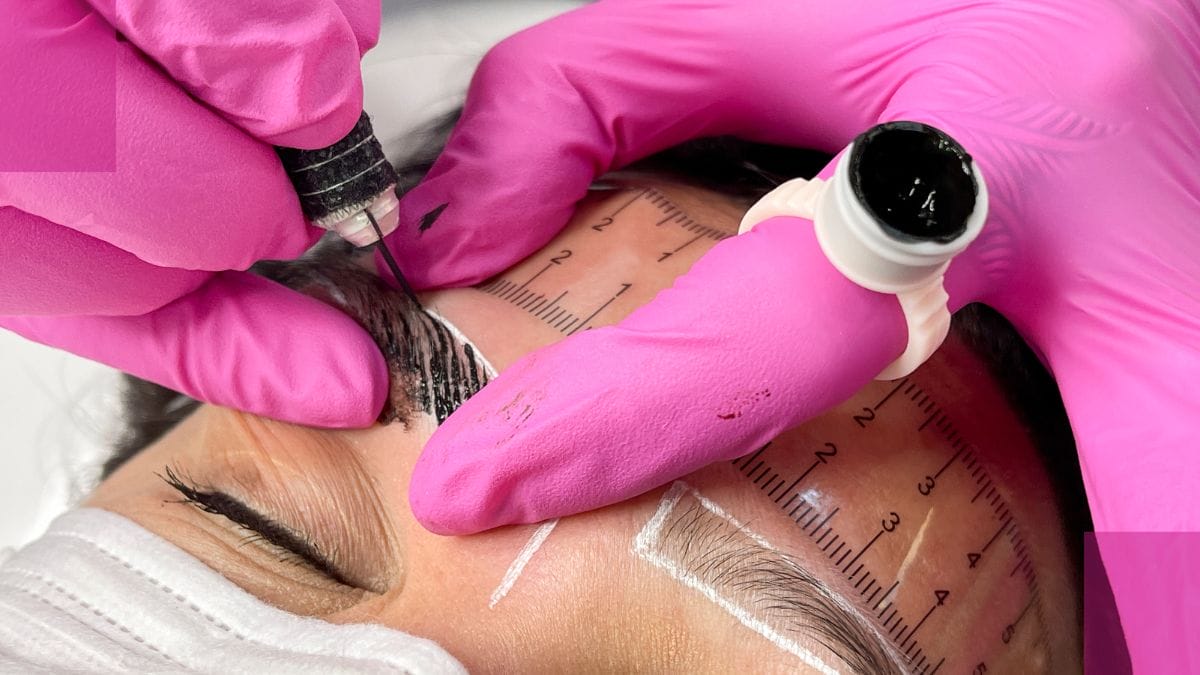 A microblading artist carefully tattoos her client's eyebrows.