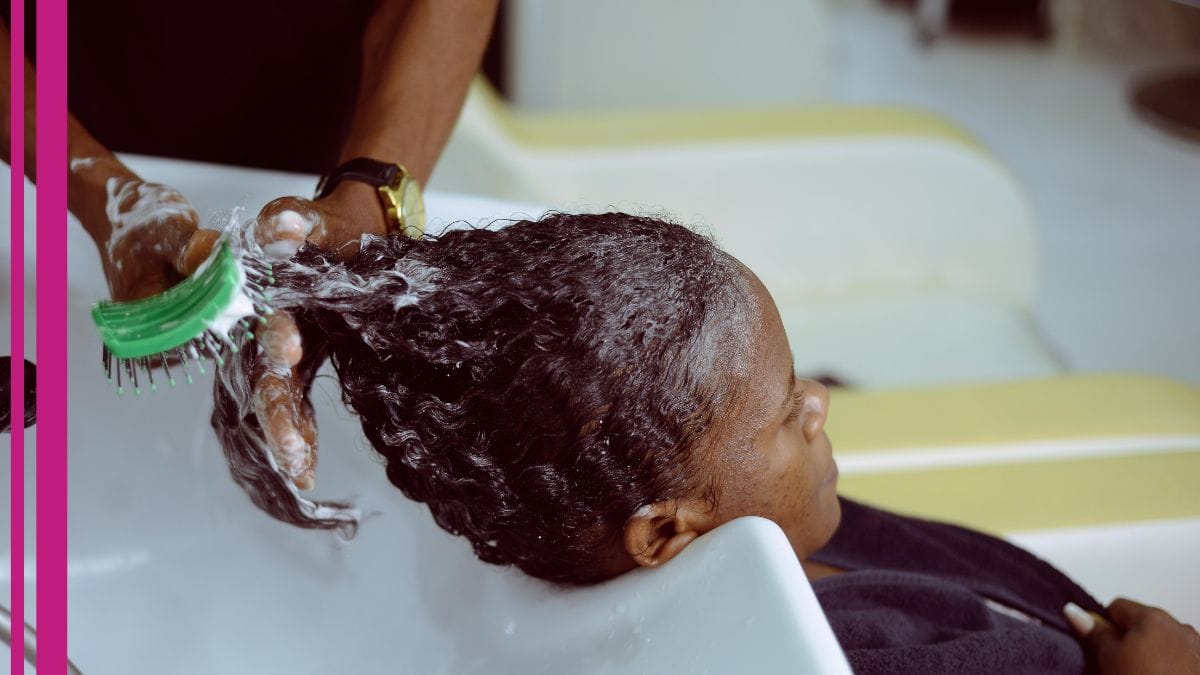 A stylist washes her clients hair while answering her client's question about how much does a cosmetologist make?