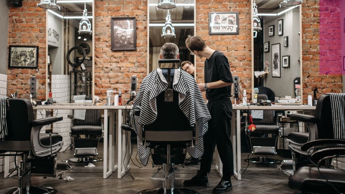 A client looks into the mirror with his barber, pondering barber liability insurance coverage options.