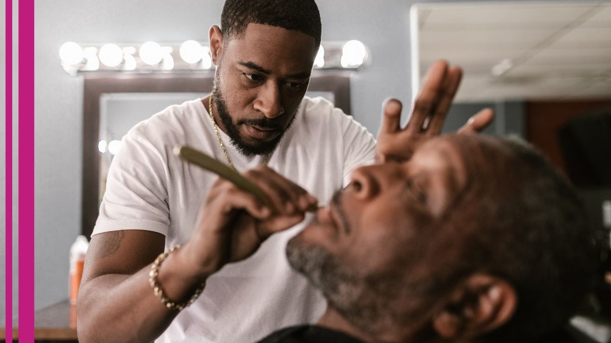 A barber works on his client's beard carefully with barber liability insurance in his back pocket.